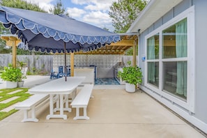 A covered patio with a table and benches, a grill, and potted plants.