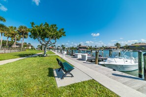 A marina with boats docked, a grassy area with a bench, and a clear blue sky.