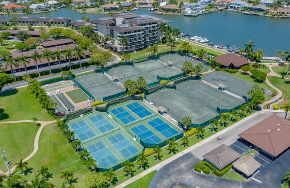 An aerial view of a hotel complex with multiple tennis courts, a marina, and surrounding greenery.