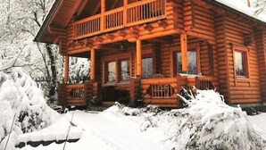 Una cabaña de troncos con balcón, rodeada de árboles cubiertos de nieve.