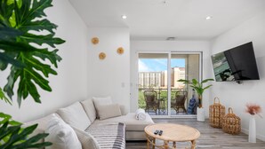 Un salon moderne avec un canapé, une table ronde en osier et un téléviseur fixé au mur.