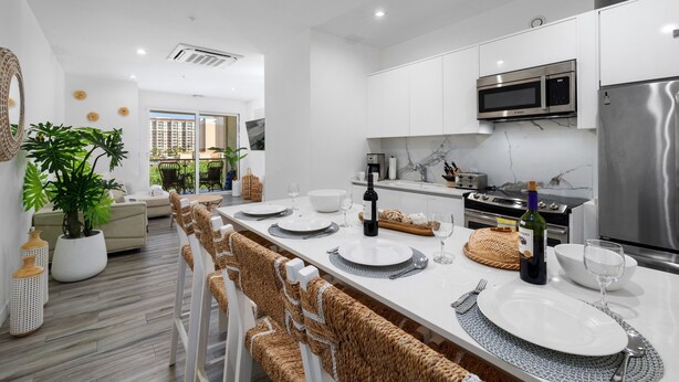 Une cuisine moderne avec des meubles blancs, des appareils en acier inoxydable et un coin repas doté d’une longue table dressée pour six personnes.