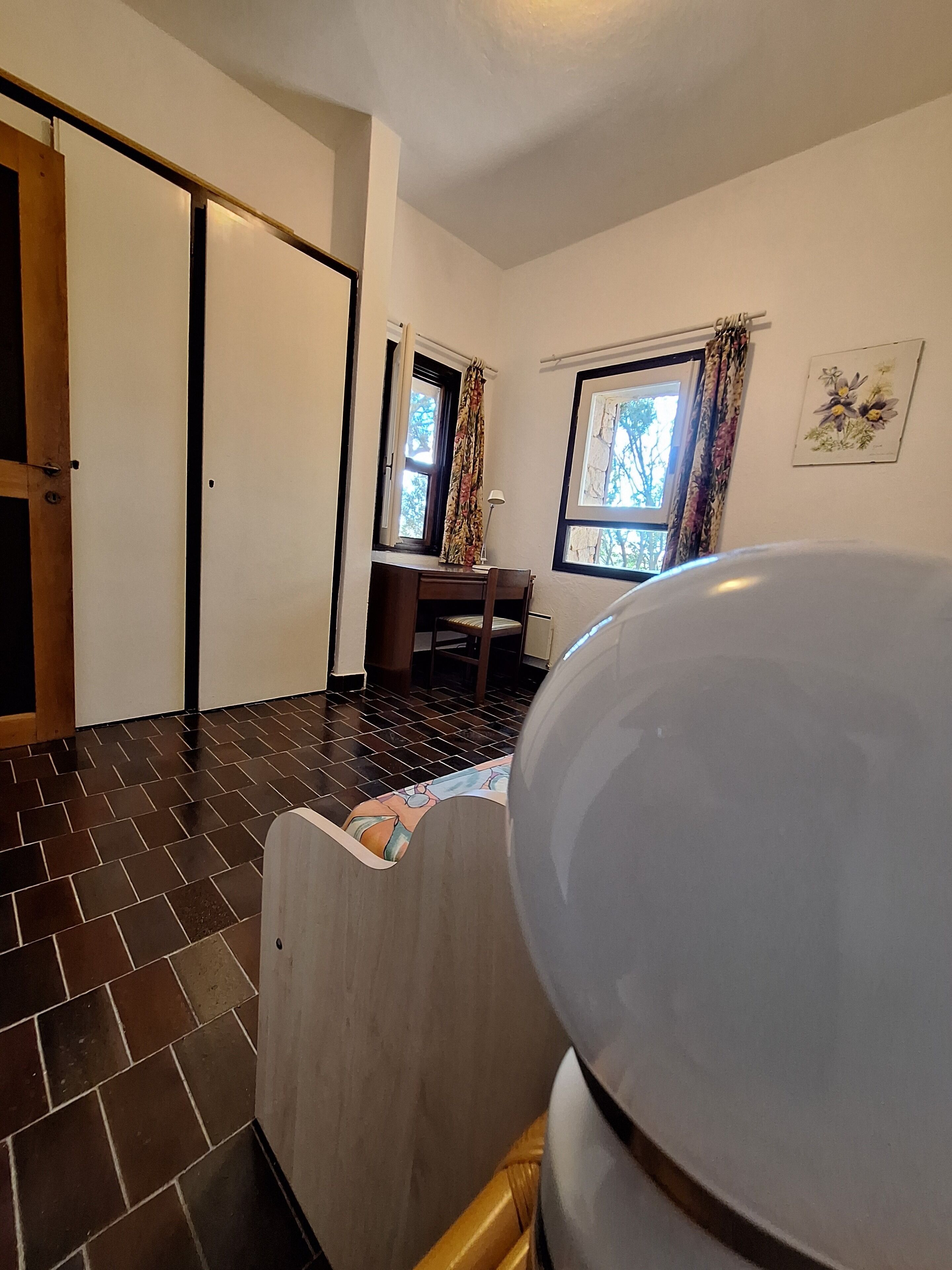 Une pièce avec un sol carrelé, un bureau avec une chaise, une fenêtre avec des rideaux et une porte.
