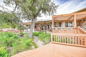 Une terrasse en bois avec un chemin de pierre menant à un bâtiment doté d’un espace extérieur aménagé et d’une pergola.