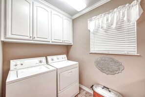 A laundry room with a washing machine, dryer, and a wall-mounted laundry sign. - Hill Country Oasis-Deck-BBQ Grill-10 Min to Town! (Fredericksburg)