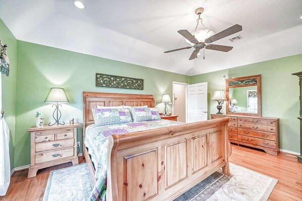 A bedroom with a wooden bed, two nightstands, a dresser, a ceiling fan, and a door.
