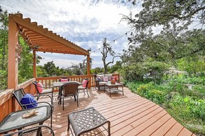 A wooden deck with outdoor furniture, including chairs and tables, surrounded by greenery.