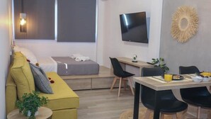 Een moderne woonkamer met een bank, een eettafel, een televisie en een kleine plant.