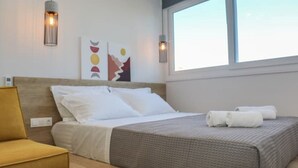 Een net opgemaakt bed met wit en grijs beddengoed, twee wandlampen en abstracte decoratie aan de muur.