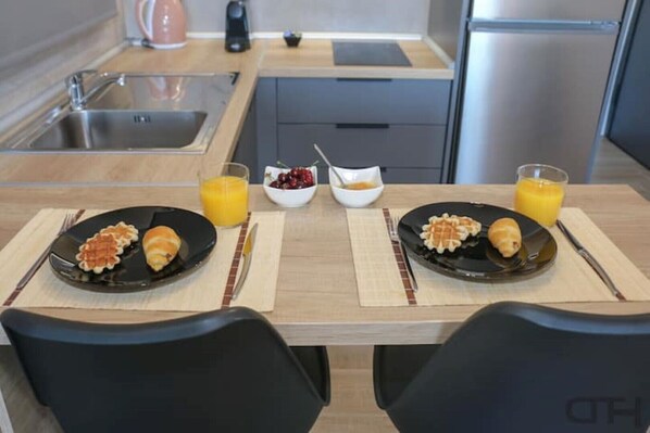 Une cuisine moderne avec deux assiettes noires contenant des gaufres et des croissants, deux verres de jus d’orange et un bol de cerises.