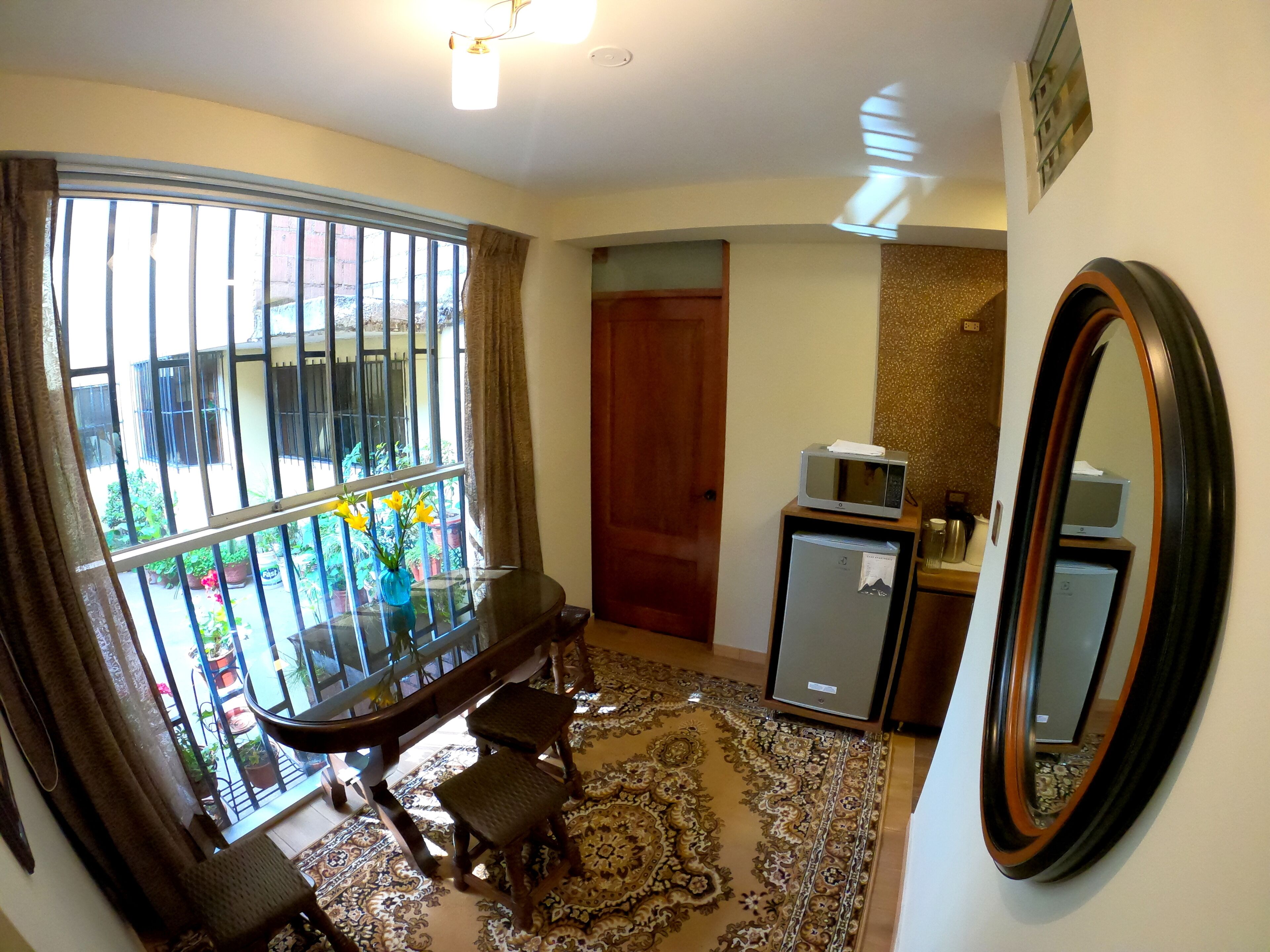 A hotel room with a balcony, a small refrigerator, a microwave, a wooden door, and a patterned rug.