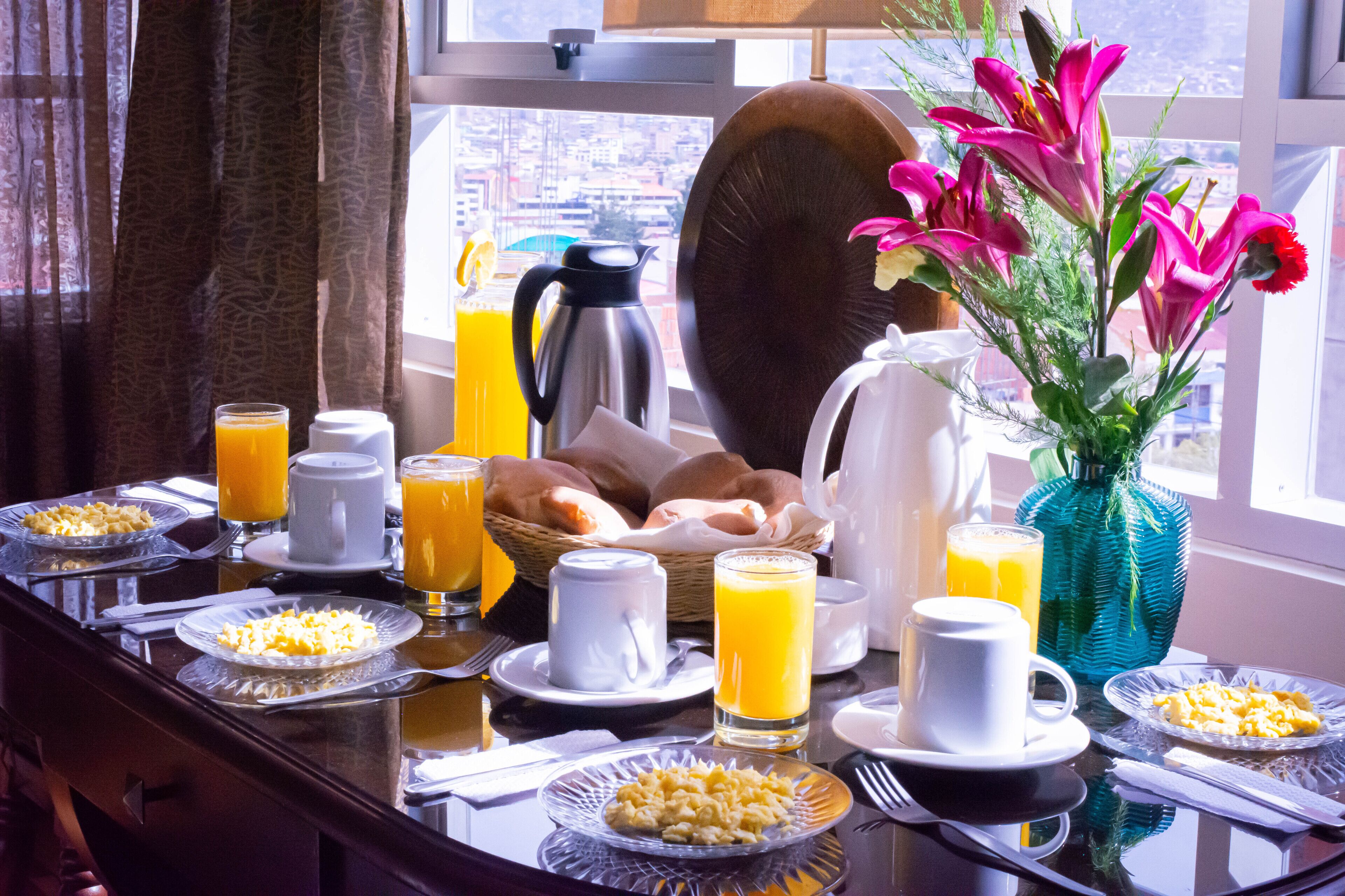 A breakfast table with plates of cereal, toast, and fruit, accompanied by glasses of orange juice and a vase of flowers.