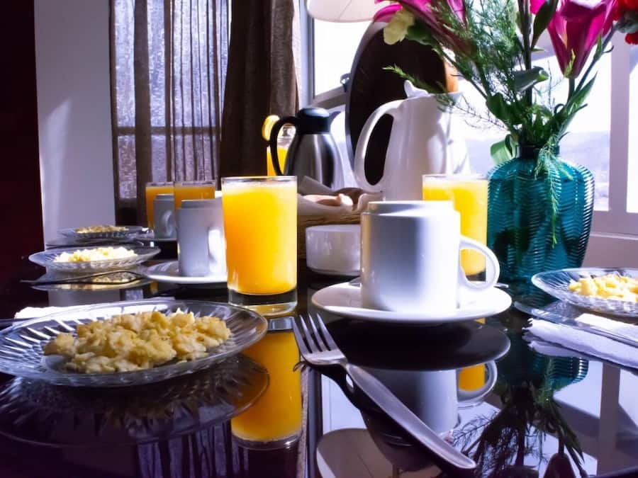 A breakfast table with plates of eggs, toast, and orange juice, along with a coffee maker and a vase with flowers.