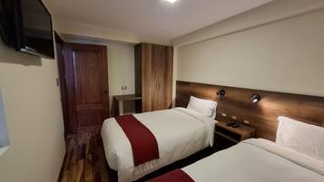 A hotel room with two beds, wooden wardrobe, bedside tables, and a TV mounted on the wall.