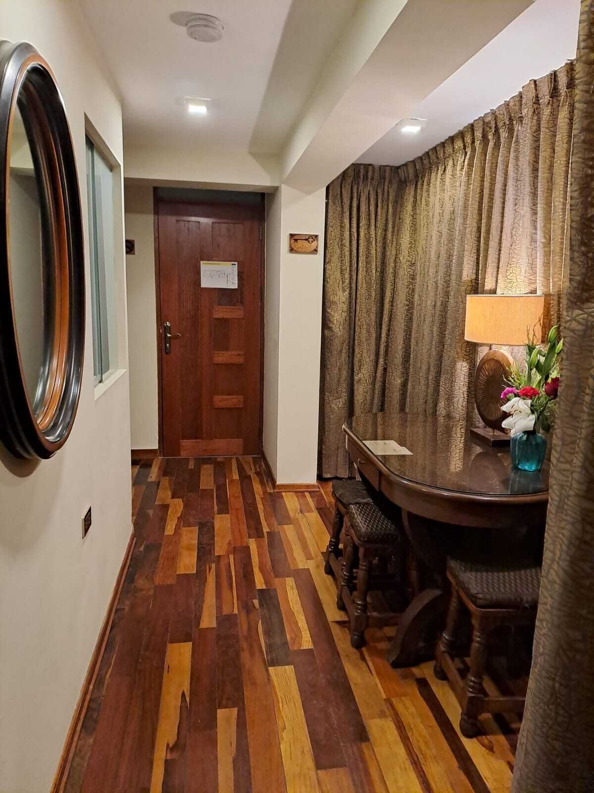 A hallway with a wooden parquet floor, a wooden door, and a dining area with a table, chairs, and a lamp.