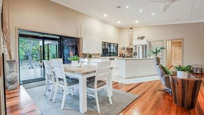 A modern kitchen with a central island, white cabinetry, and a dining area with a table and chairs. - Villa Damai -  Sunrise 1770 (Agnes Water)