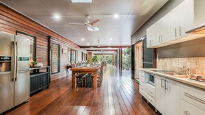 A modern kitchen with wooden flooring, a dining area, and a view of the outdoors. - Villa Damai -  Sunrise 1770 (Agnes Water)