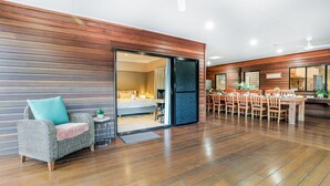 A modern hotel room with a wooden interior, a dining area with wooden tables and chairs, and a large window. - Villa Damai -  Sunrise 1770 (Agnes Water)