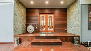 A wooden porch with a stone wall, a large door, and a stone sculpture. - Villa Damai -  Sunrise 1770 (Agnes Water)