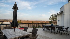 Eine Terrasse im Freien mit Holztisch und Korbstühlen, mit Blick auf einen Weinberg.