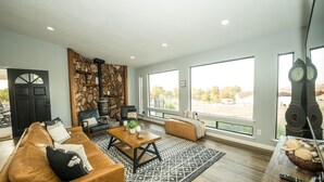 Ein geräumiges Wohnzimmer mit braunem Ledersofa, einem Holztisch und einem großen Fenster mit Blick ins Freie.