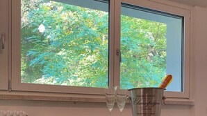A dining area with a table, two chairs, a window with a view of greenery, and a champagne bucket. - Spacious and bright apartment surrounded by greenery 10 minutes from Varese (Valganna)