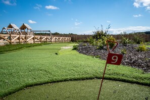 A golf course with a well-maintained green, a wooden fence, and a red flag marking the 9th hole.