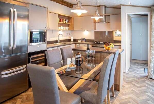 A modern kitchen with stainless steel appliances, a glass dining table, and grey upholstered chairs.