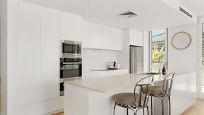 Een moderne keuken met witte kastjes, roestvrijstalen apparatuur en een centraal eiland met barstoelen.
