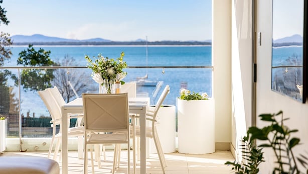 Een balkon met een tafel en stoelen, met uitzicht op een waterpartij en bergen.