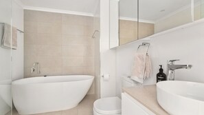 Een moderne badkamer met een vrijstaand bad, toilet en een wastafel met spiegel.