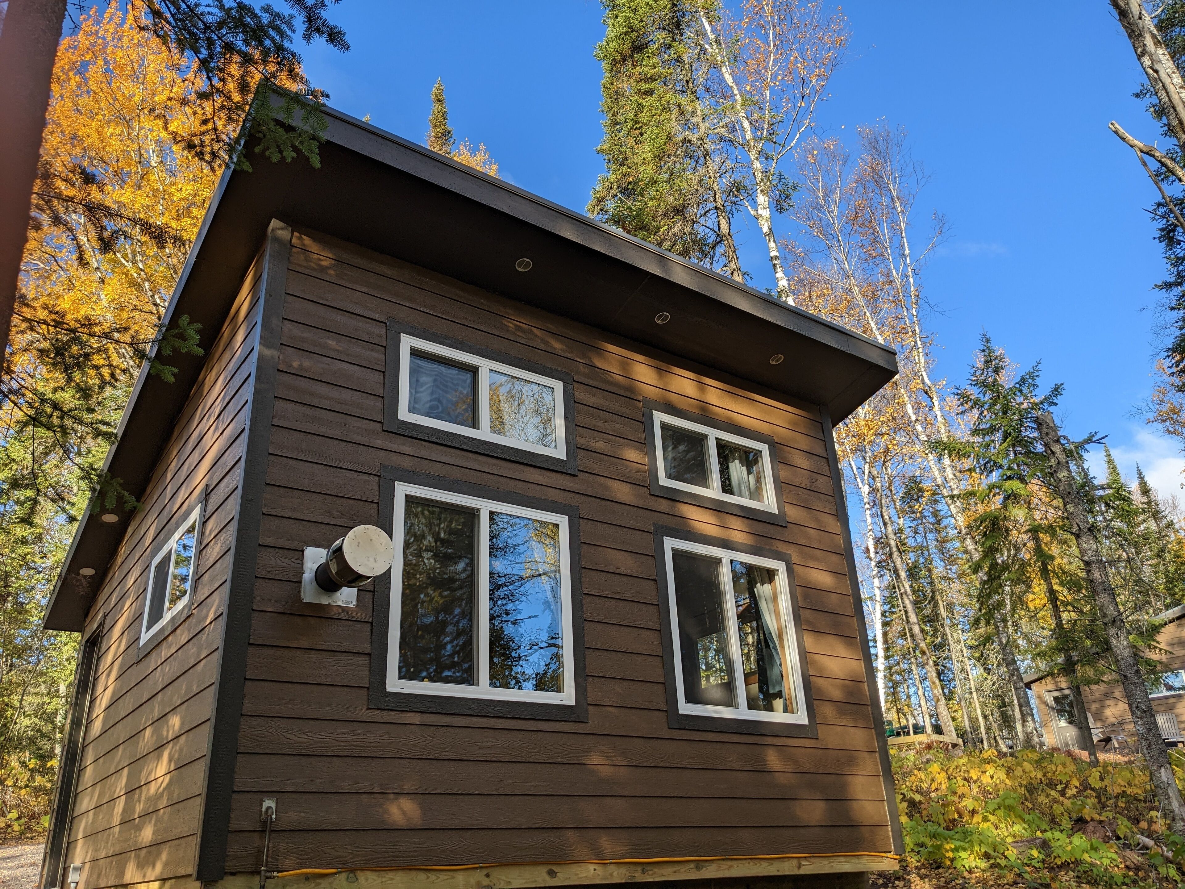 A two-story wooden cabin with multiple windows, surrounded by trees and a clear sky.