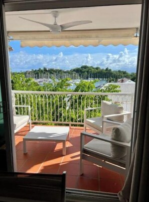 Un balcon doté d’un ventilateur de plafond blanc, de mobilier d’extérieur blanc et offrant une vue sur une marina et sur la verdure.