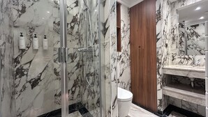 Moderni kylpyhuone, jossa on marmoriseinät, lasiseinäinen suihku, puinen allaskaappi ja wc.