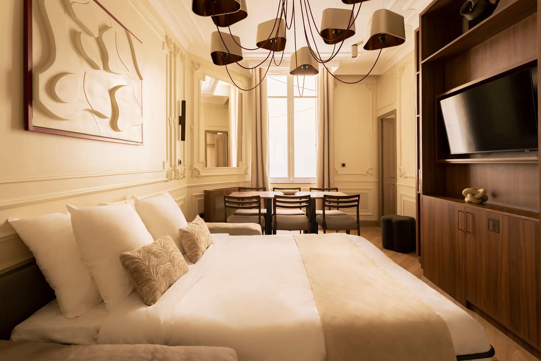 A hotel room with a large bed, a dining table with chairs, a TV, and a mirror.