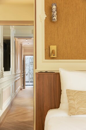 A hotel room with a wooden headboard, a bed with white linens, a nightstand, a wall-mounted light, and a mirror. - Luxury Suite - Champs Elysees - Wagram (Paris)