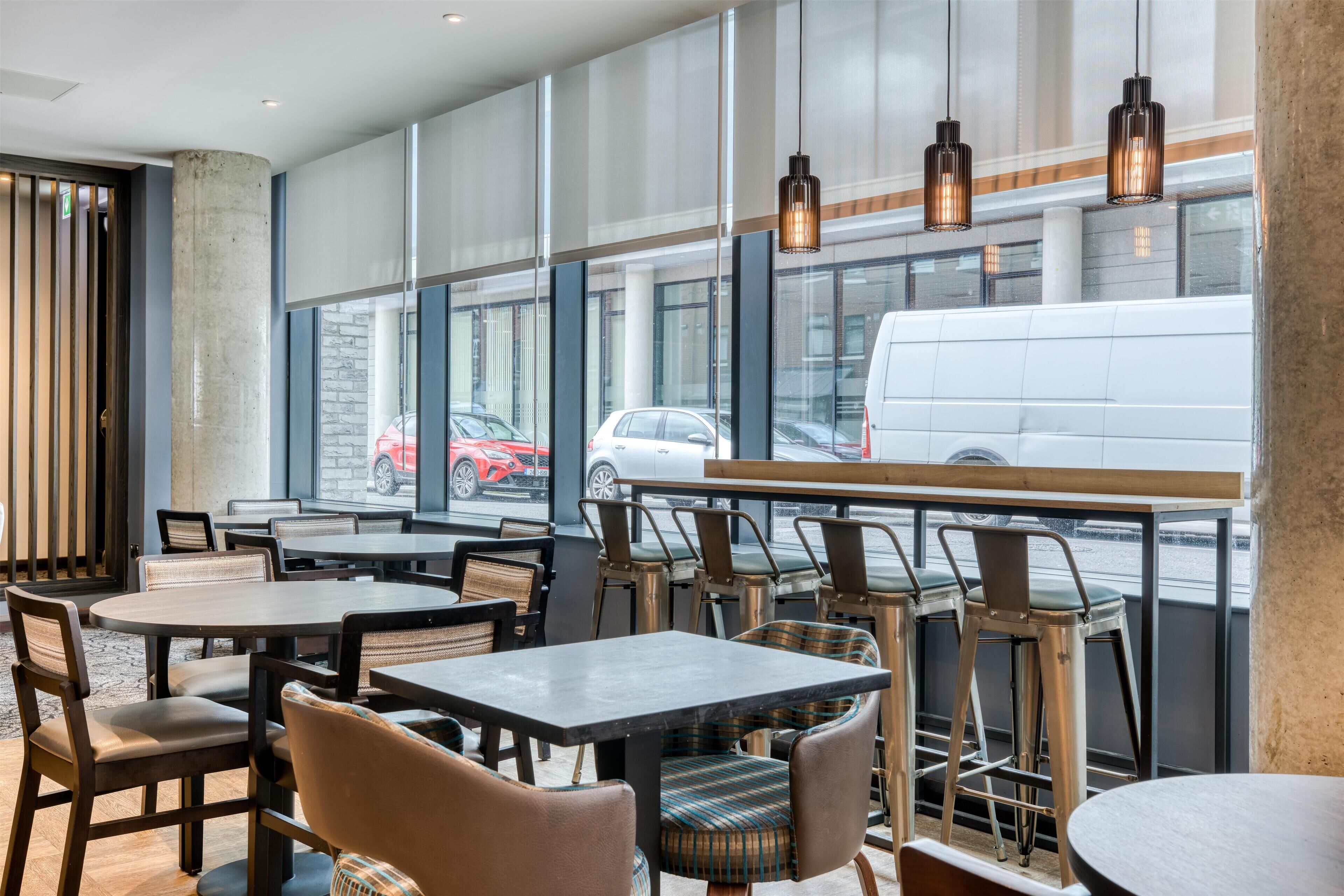 A modern restaurant with large windows, wooden tables, and metal chairs.