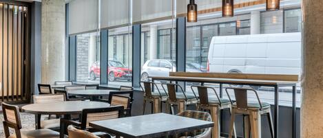 A modern restaurant with large windows, wooden tables, and metal chairs.