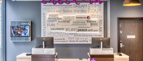 A hotel reception area with a check-in counter, a wall with motivational phrases, and a television displaying the hotel.
