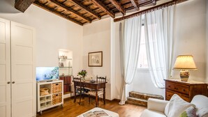 Un salon chaleureux avec un plafond en bois, un canapé blanc, une table à manger avec des chaises, un petit meuble et une lampe.