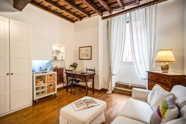 Ein gemütliches Wohnzimmer mit Holzbalkendecke, einem weißen Sofa, einem Esstisch mit Stühlen, einer kleinen Kommode und einer Lampe.