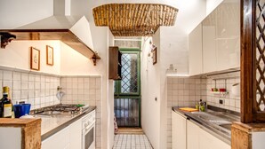 Une cuisine de taille réduite avec des murs recouverts de carreaux blancs, une cuisinière à gaz et un plafond en bois.