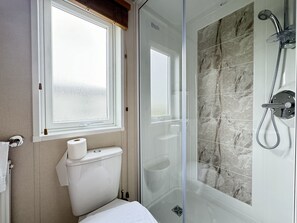 Et badeværelse med toilet, glasvæg omkring brusenichen og et vindue.