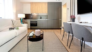 A modern living room with a sofa, a coffee table, and a dining area with chairs. A kitchen with cabinets and appliances is visible in the background. - Genteel Home Arruzafa I (Cordoba)