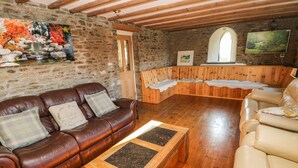 A cozy room with a stone wall, wooden ceiling beams, a brown leather sofa, a wooden coffee table, and a wooden bench. - Nant Moel Isaf Farm (Swansea)
