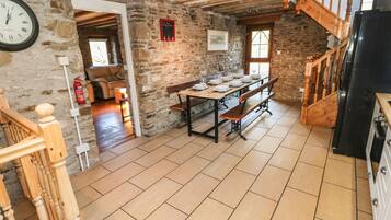 Un comedor rústico con una mesa de madera dispuesta para cuatro personas, un muro de piedra y una escalera de madera.