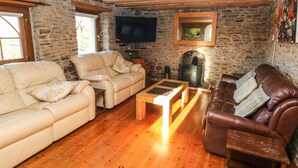 A cozy living room with a stone wall, a fireplace, a television, and two sofas. - Nant Moel Isaf Farm (Swansea)