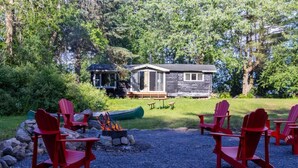 Uma cabana com lareira e cadeiras Adirondack vermelhas numa área arborizada.