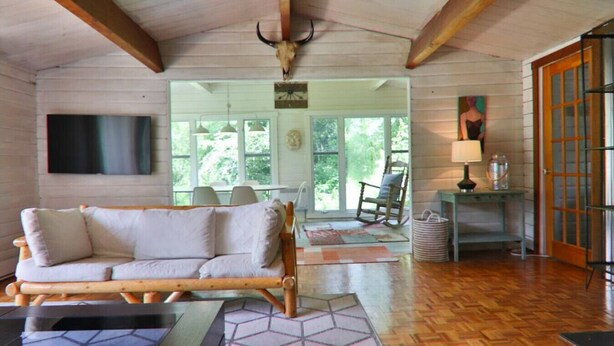 Interior acolhedor de uma cabana com teto de madeira, um sofá, uma mesa de jantar e uma poltrona de balanço.
