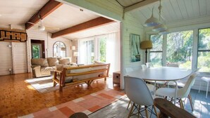 Uma sala de estar ampla com um banco de madeira, uma mesa de jantar com cadeiras e uma janela grande com vista para o verde lá fora.